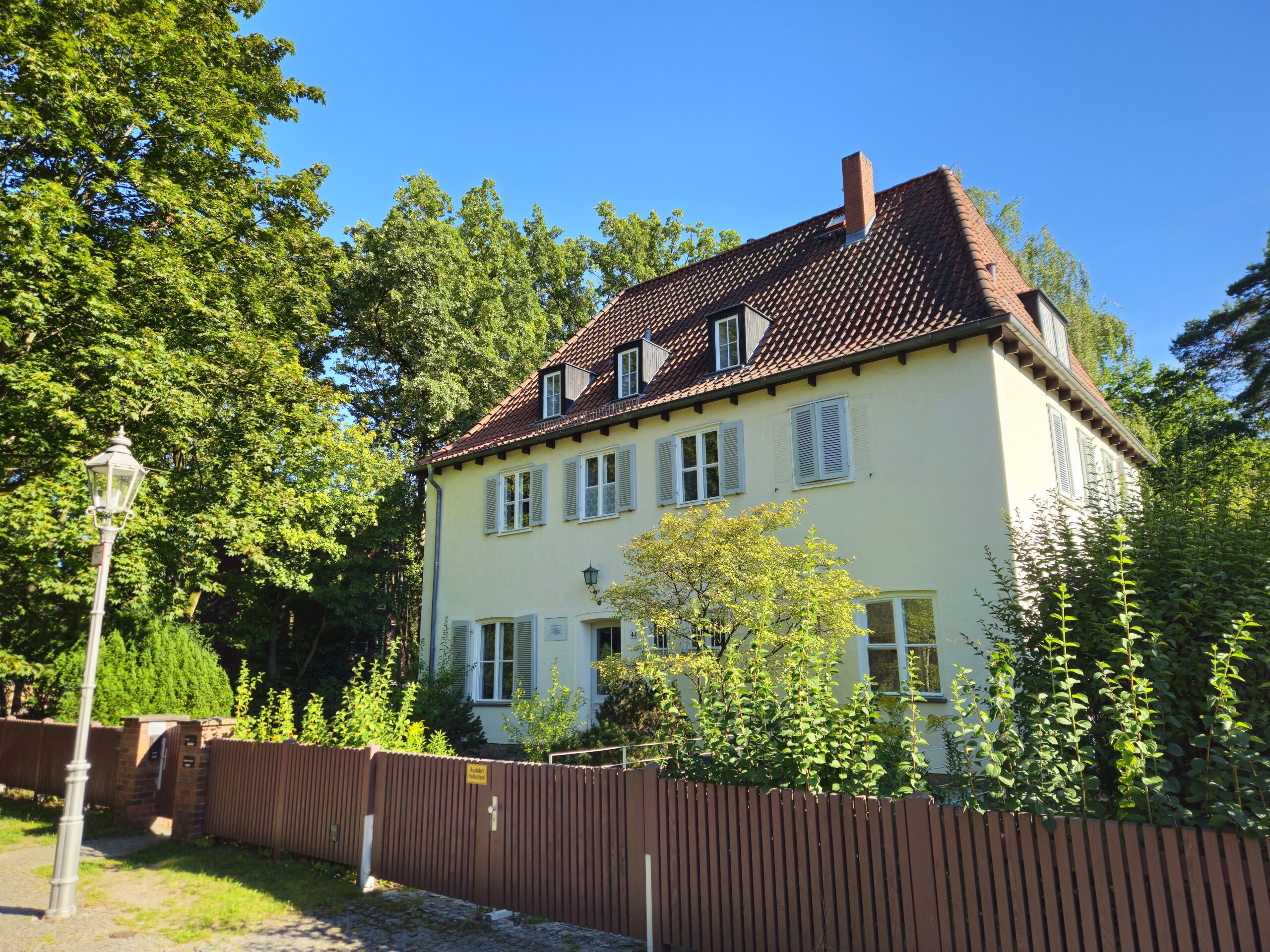 Das Bild zeigt die Straßenansicht des Bonhoeffer-Hauses in Berlin-Charlottenburg, eine klassische Fassade mit Vorgarten und Eingangstür. The picture shows the street view of the Bonhoeffer House in Berlin-Charlottenburg, featuring a classic façade with a front garden and entrance door.