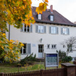 Das Bild zeigt die Straßenansicht des Bonhoeffer-Hauses in Berlin-Charlottenburg, eine klassische Fassade mit Vorgarten und Eingangstür. The picture shows the street view of the Bonhoeffer House in Berlin-Charlottenburg, featuring a classic façade with a front garden and entrance door.
