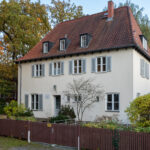 Das Bild zeigt die Straßenansicht des Bonhoeffer-Hauses in Berlin-Charlottenburg, eine klassische Fassade mit Vorgarten und Eingangstür. The picture shows the street view of the Bonhoeffer House in Berlin-Charlottenburg, featuring a classic façade with a front garden and entrance door.