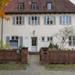 Das Bild zeigt die Straßenansicht des Bonhoeffer-Hauses in Berlin-Charlottenburg, eine klassische Fassade mit Vorgarten und Eingangstür. The picture shows the street view of the Bonhoeffer House in Berlin-Charlottenburg, featuring a classic façade with a front garden and entrance door.